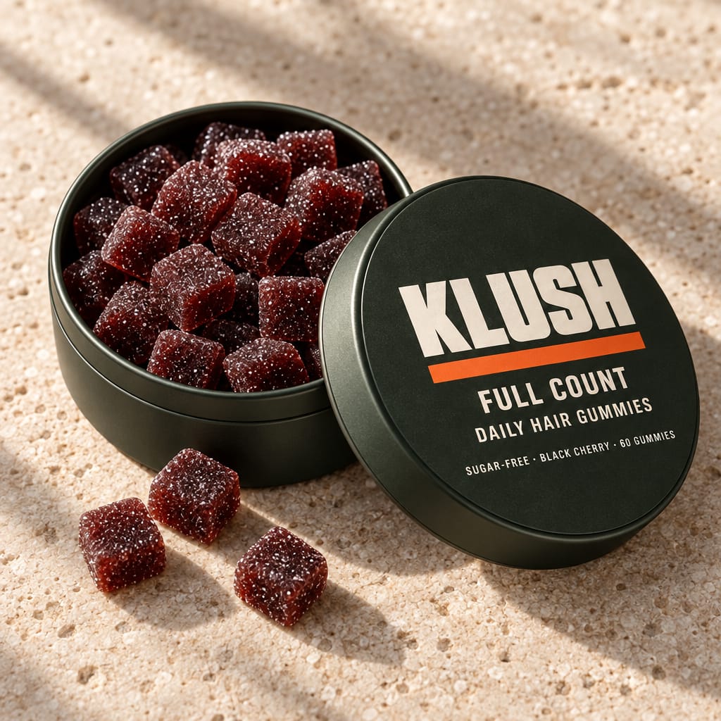 The open tin full of sugar-dusted black-cherry gummies, its lid leaning on it, on bone stone in soft daylight