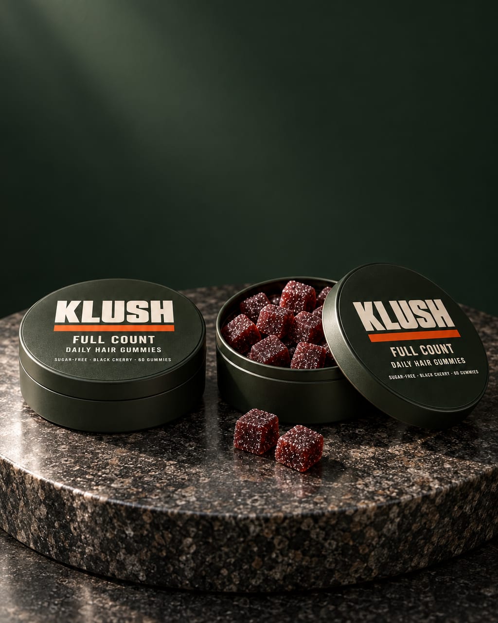 Two Full Count tins, one open and full of black-cherry gummies, on a dark granite pedestal under a soft spotlight, calm and